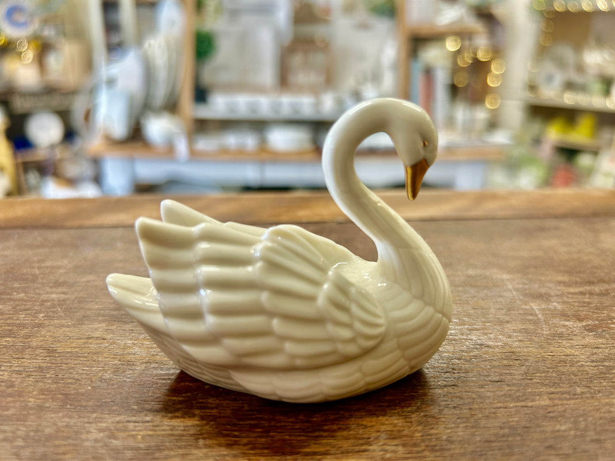 Cream porcelain swan cake topper with curved neck, upright side view on wood surface.