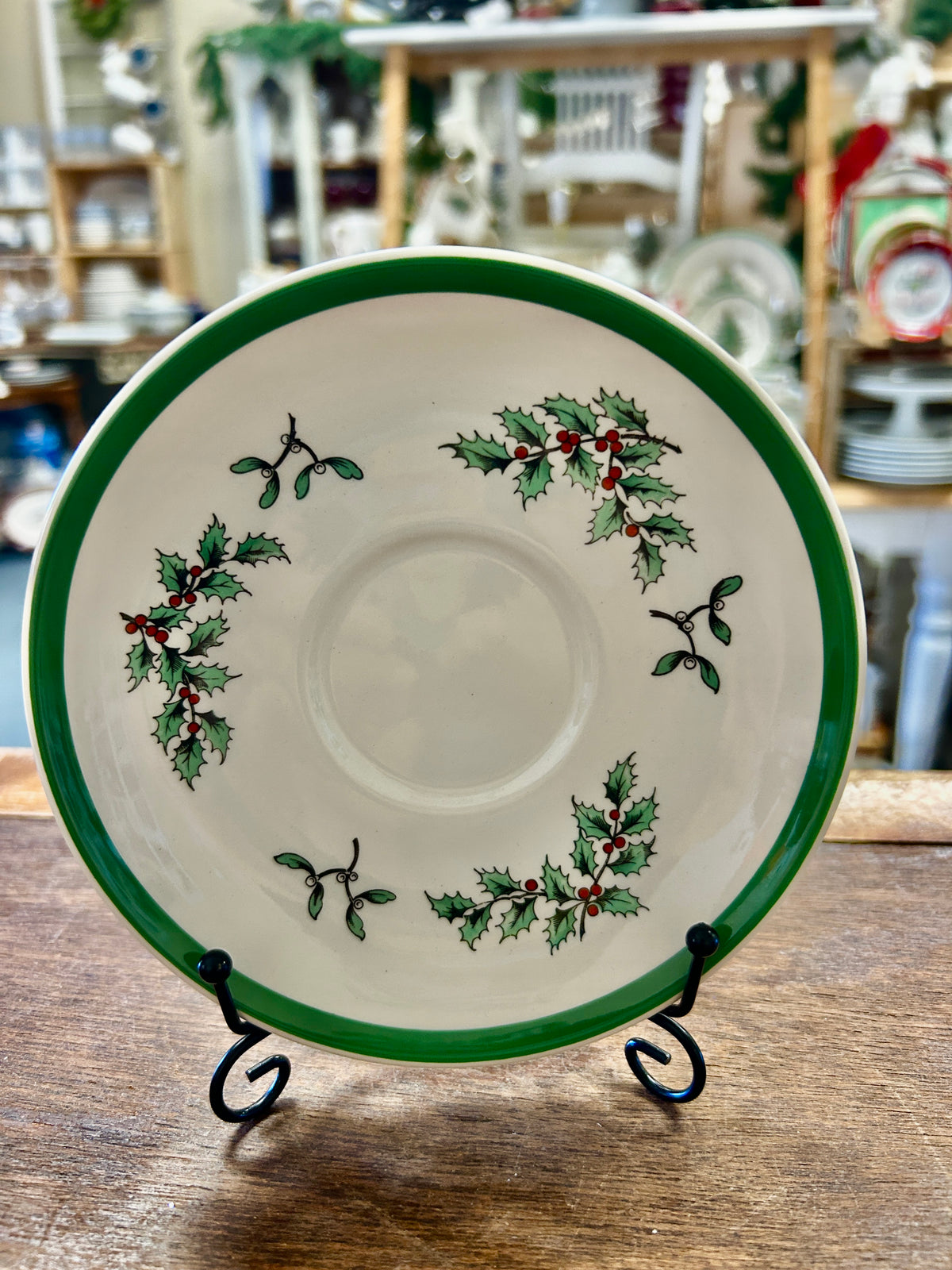 White saucer plate with green rim and circular holly sprig pattern, on stand