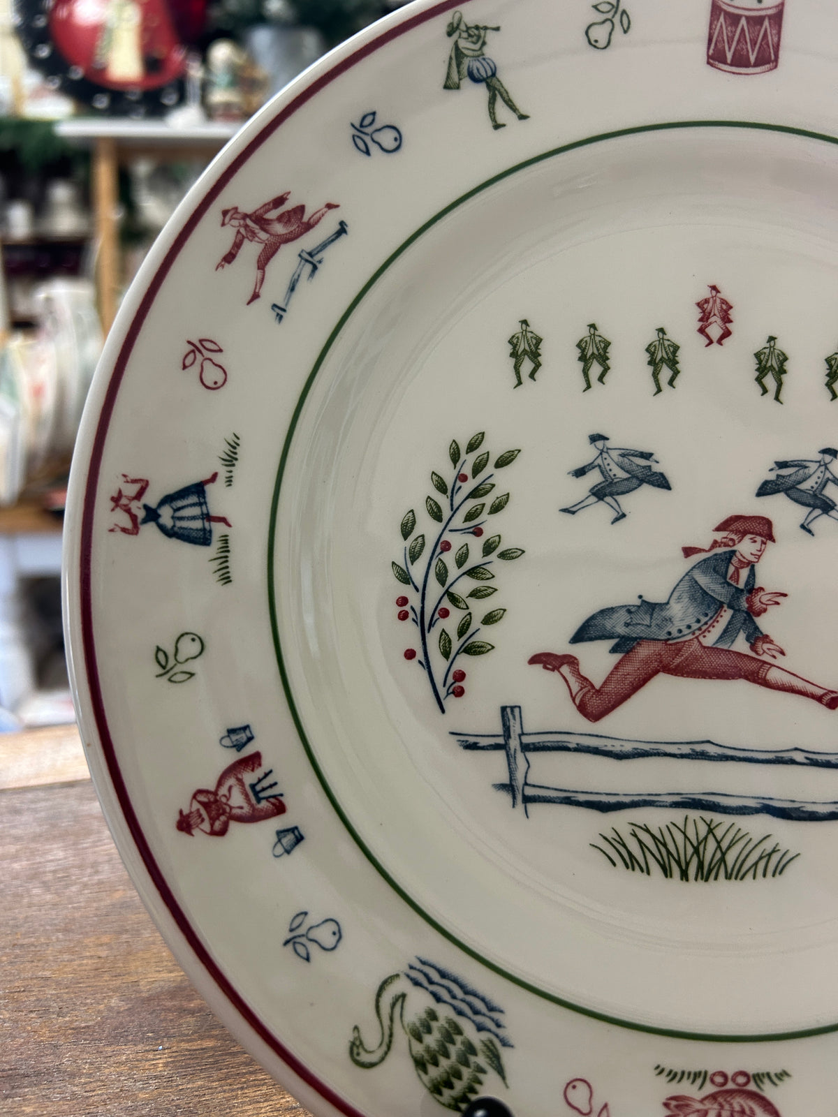 Multicolor Christmas plate detail with horse rider, fence, and wreath-like sprigs on rim