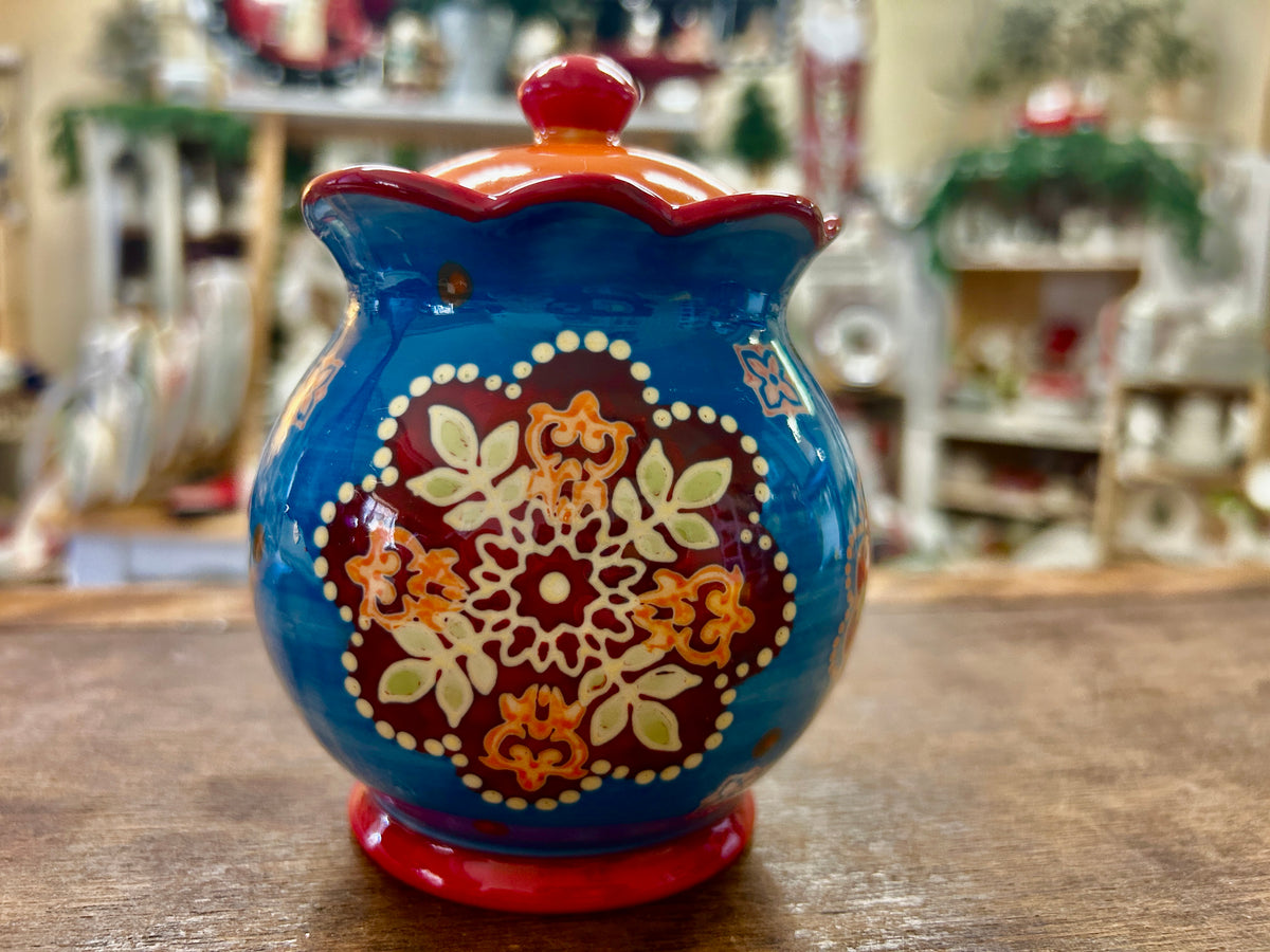 Ceramic sugar bowl with blue glaze, red lid knob, and multicolor floral Dutch wax design