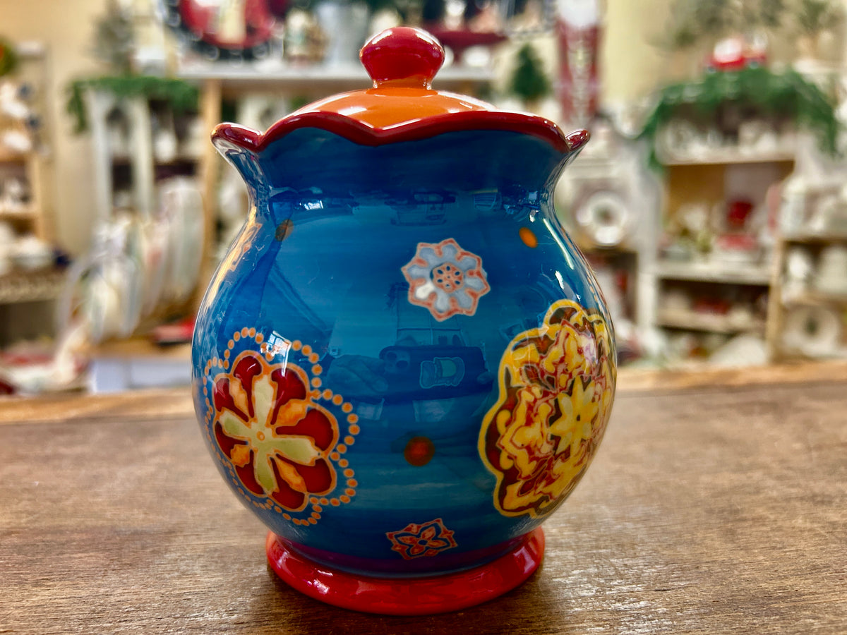 Ceramic sugar bowl with blue glaze, red lid knob, and multicolor floral pattern on front