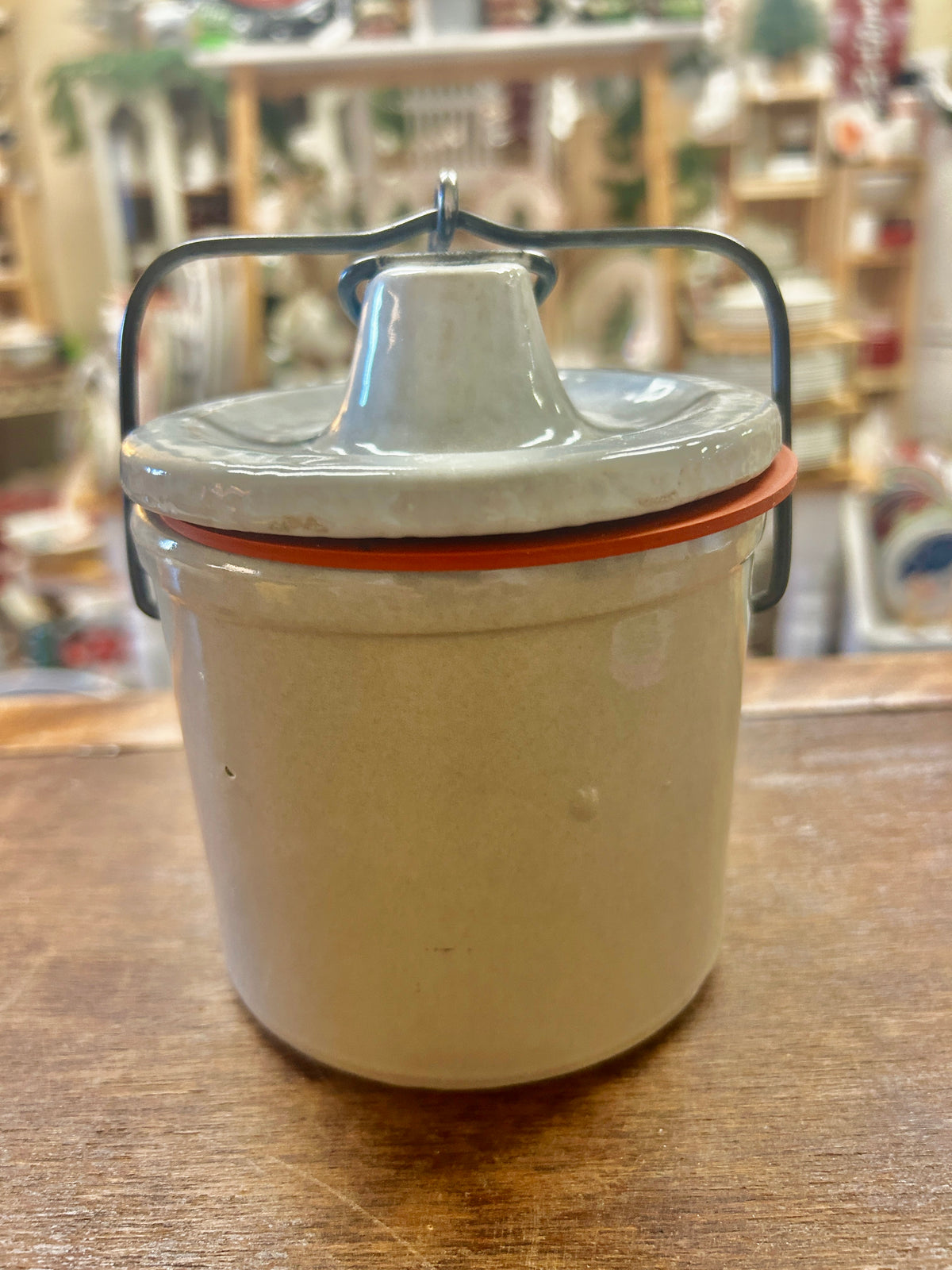 Cream stoneware crock with fitted lid, red-brown seal, and dark metal latch handle