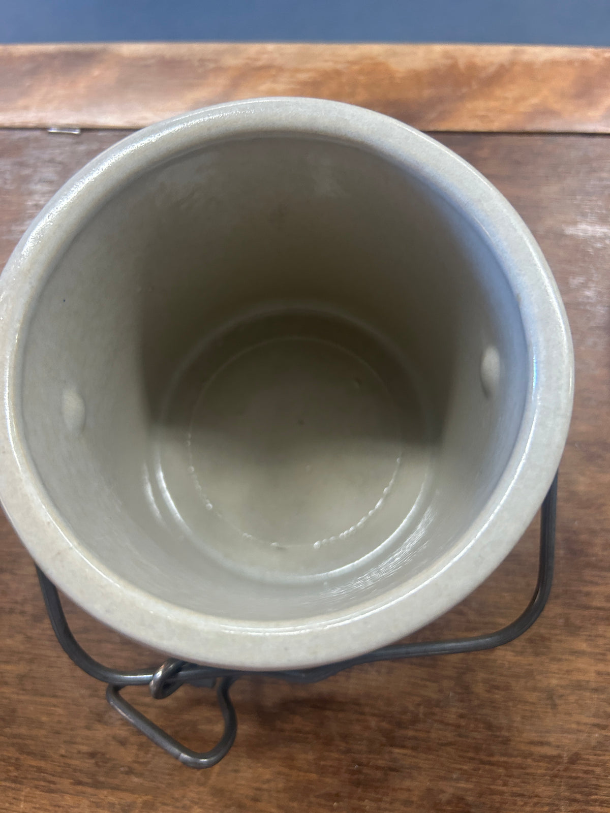 Open cream stoneware crock showing its glazed interior and dark metal latch handle