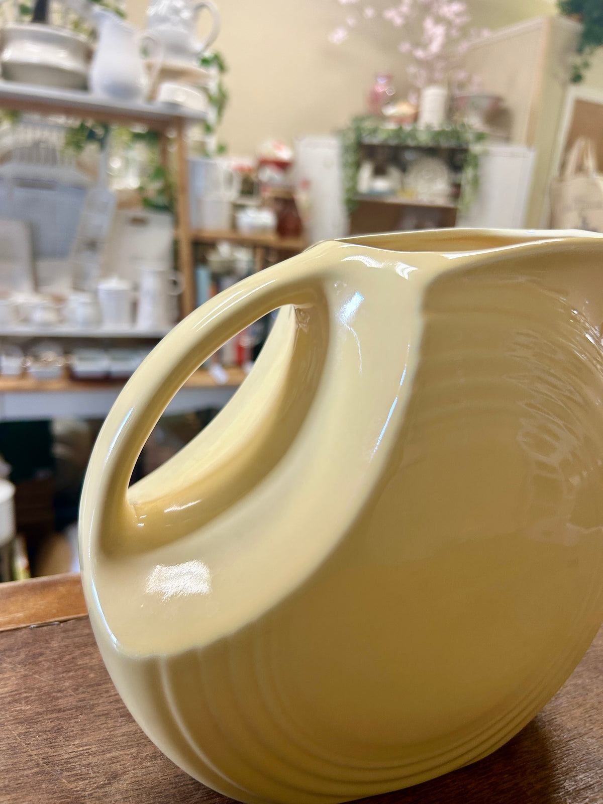 Yellow ceramic pitcher angled view, curved handle and spout detail.