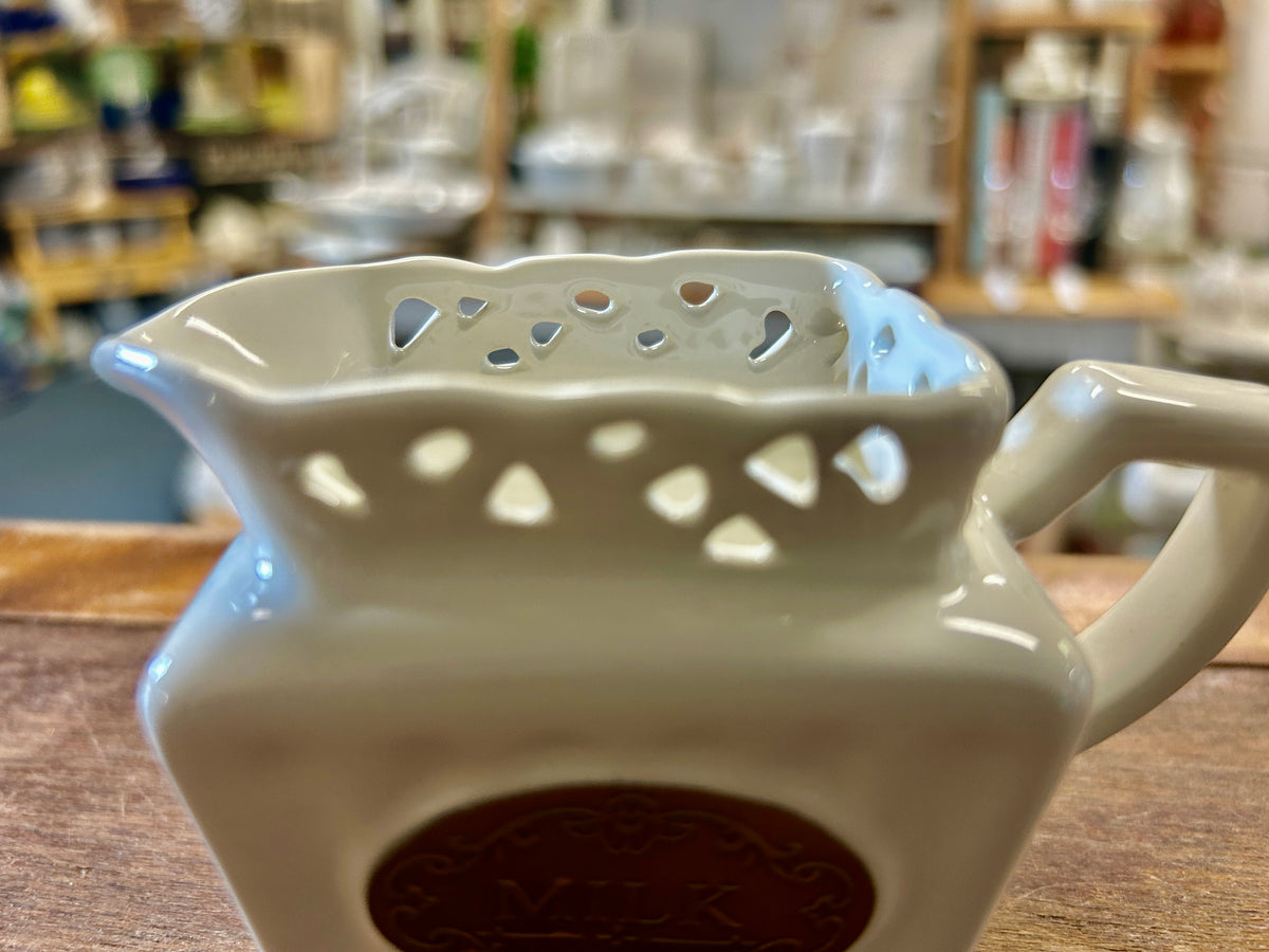 Cream ceramic milk creamer with cutout top rim, side handle, front 'MILK' medallion