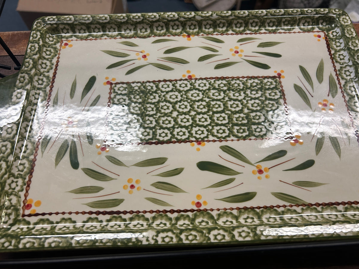 Close-up of white ceramic platter with green leaf pattern and orange flower accents