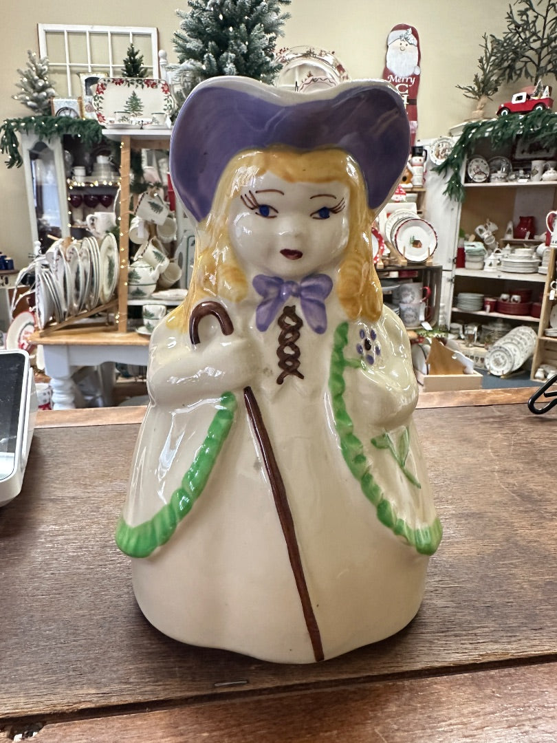 Ceramic character pitcher with painted girl figure, blue bonnet, green trim, curved handle