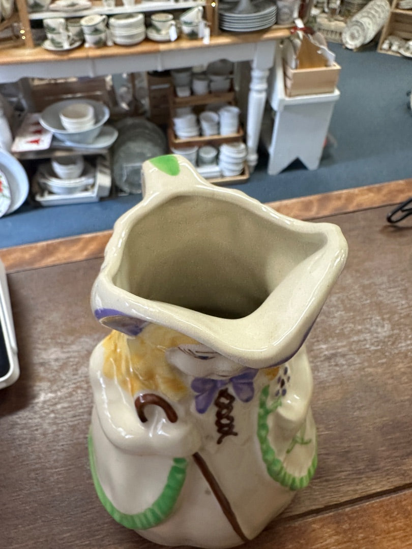 Ceramic pitcher with wide square mouth opening, painted doll details, green base rim