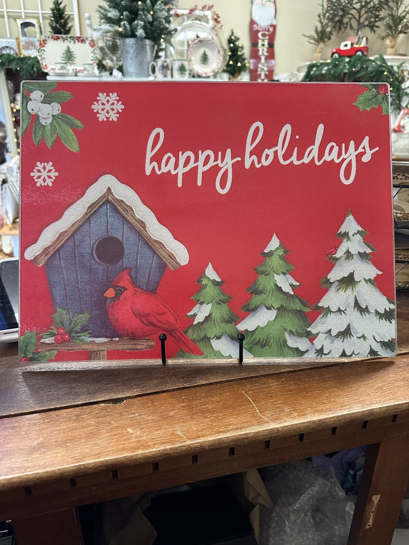 Red glass holiday board with 'Happy holidays' and cardinal, pine trees, house graphic