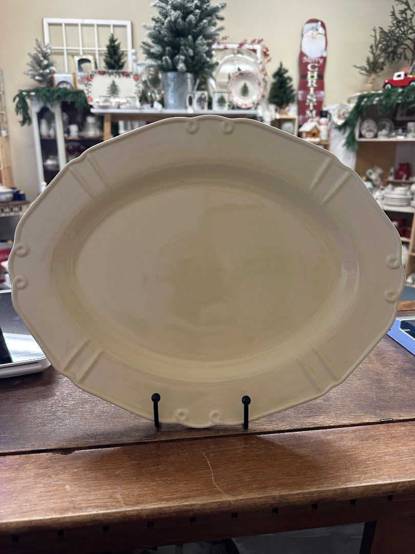 Yellow oval ceramic serving platter with raised rim and side handles on display stand
