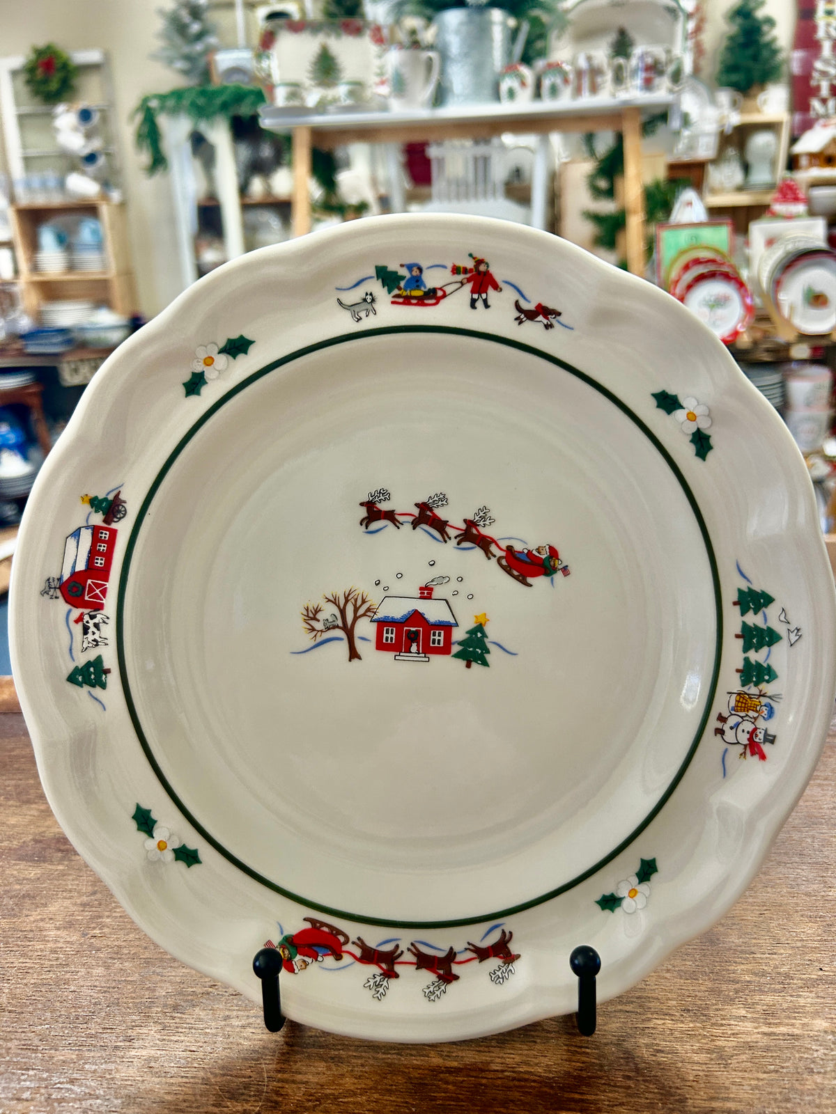 Decorative holiday scene dinner plate with red sleigh, houses, and green holly rim
