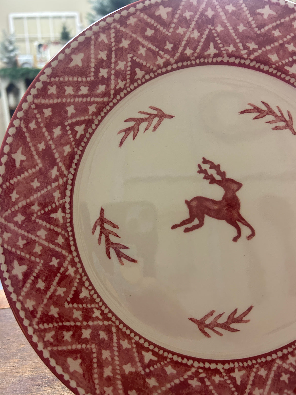 Close-up of cream dinner plate with red reindeer and leaf motifs on patterned rim