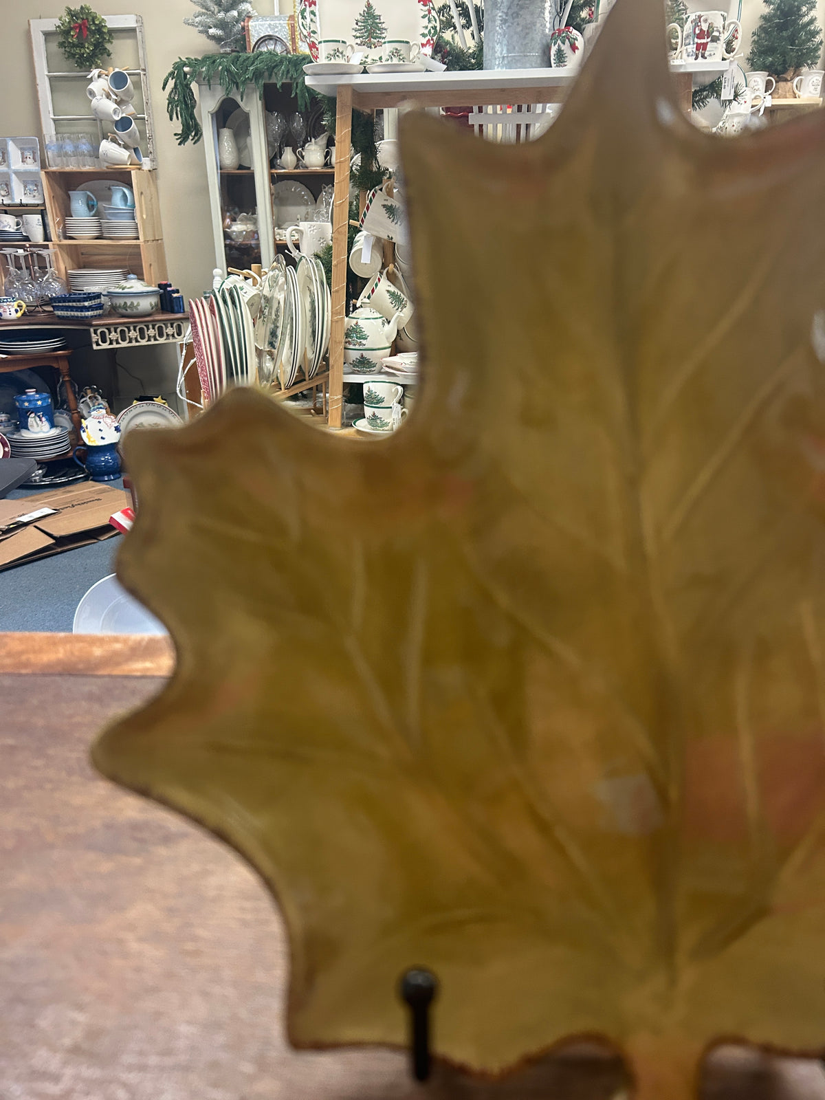 Gold-green leaf-shaped ceramic plate with raised veins, shown from a side angle on stand