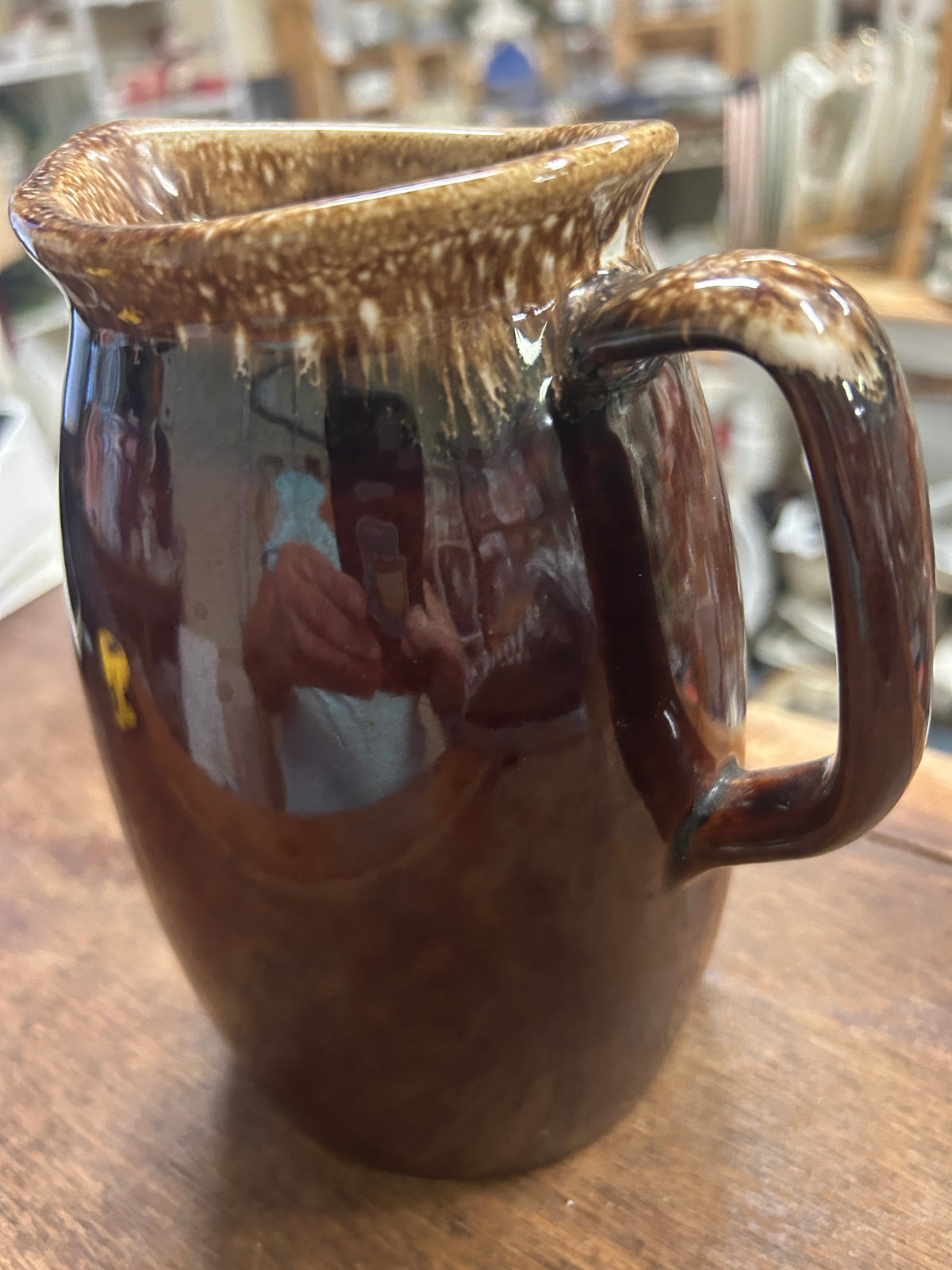 Brown ceramic pitcher with curved handle and speckled drip-glaze rim.