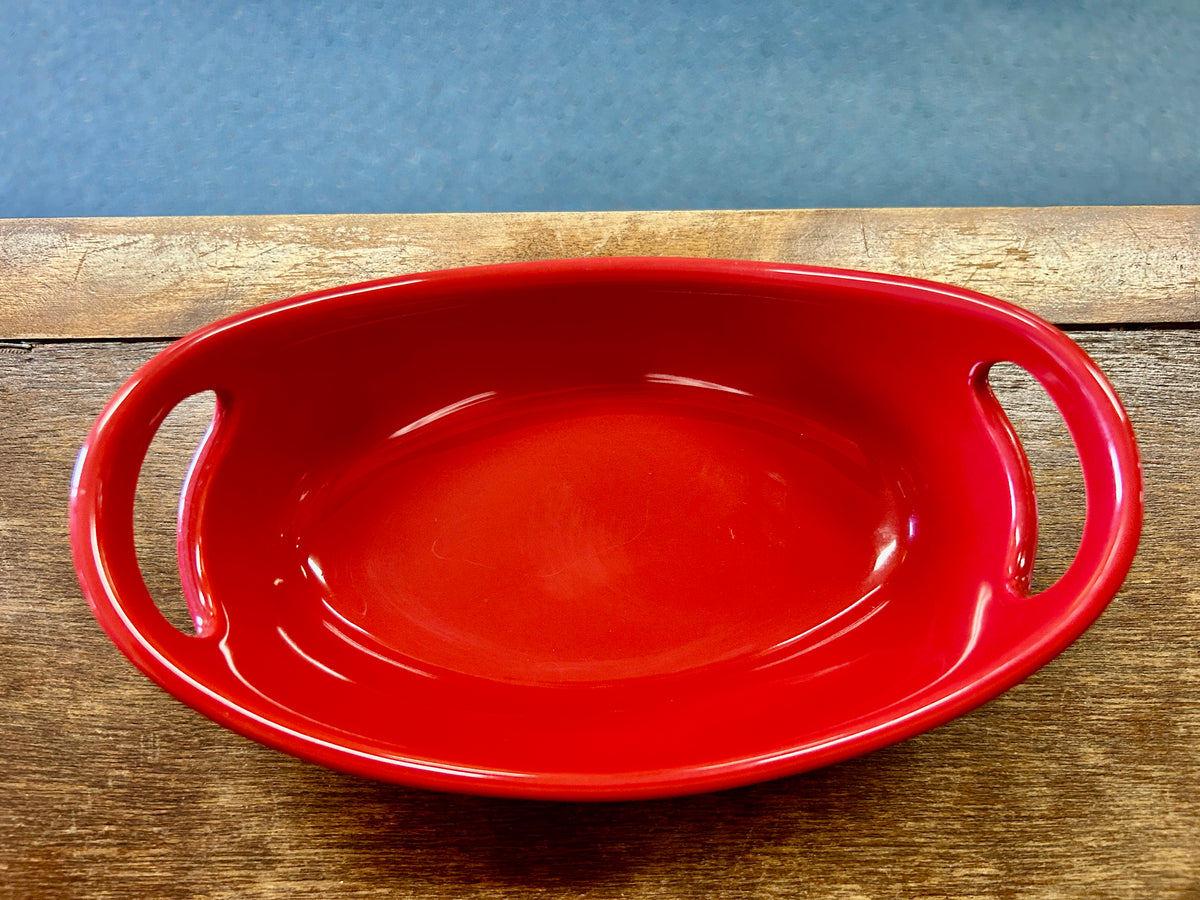Red oval ceramic bowl with two side handles, shallow serving shape