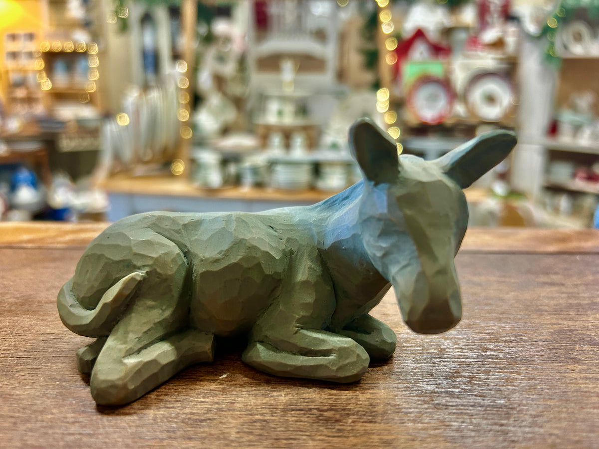 Greenish donkey nativity figurine lying on wooden tabletop