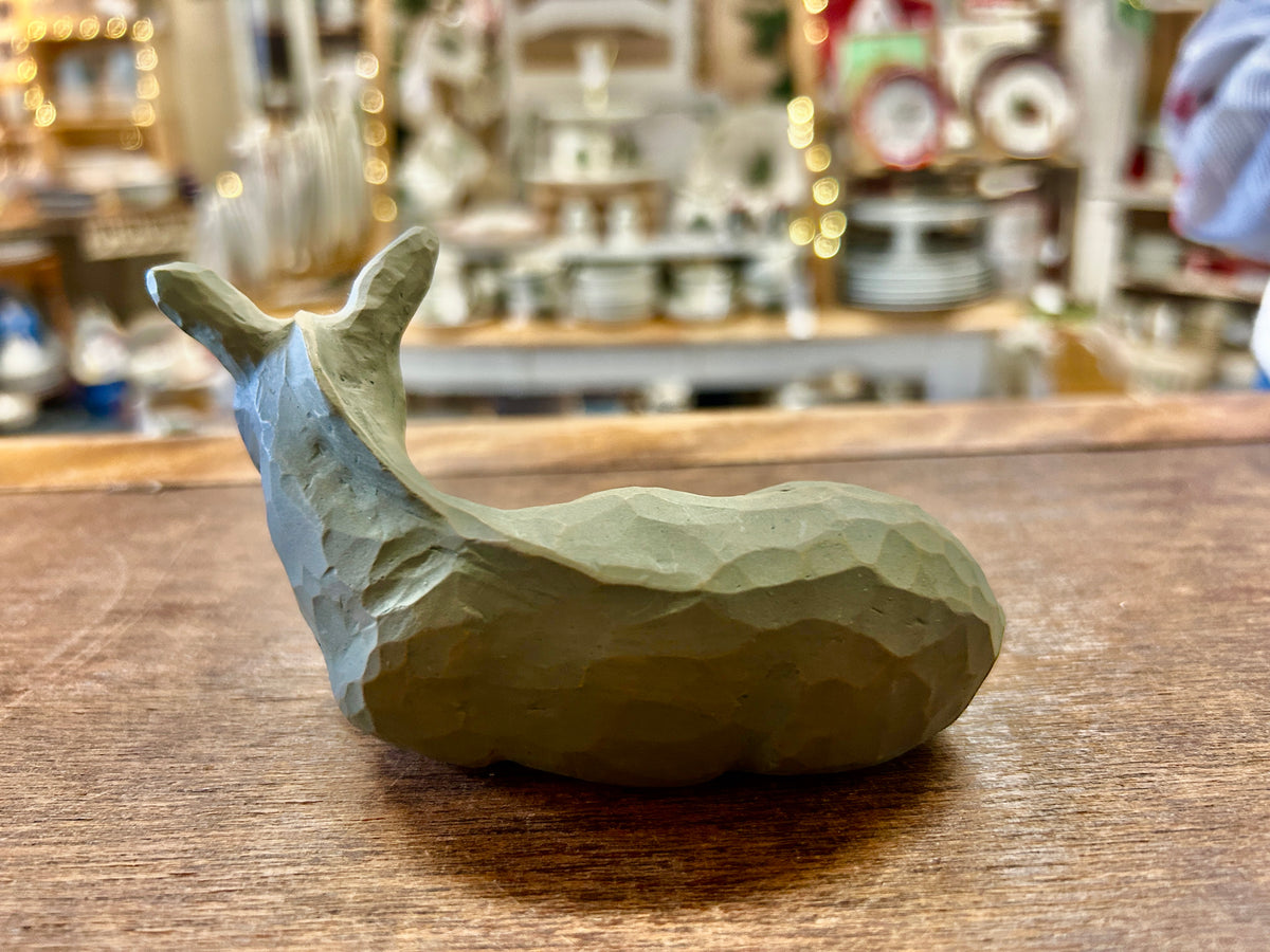 Greenish donkey nativity figurine curled on wooden tabletop