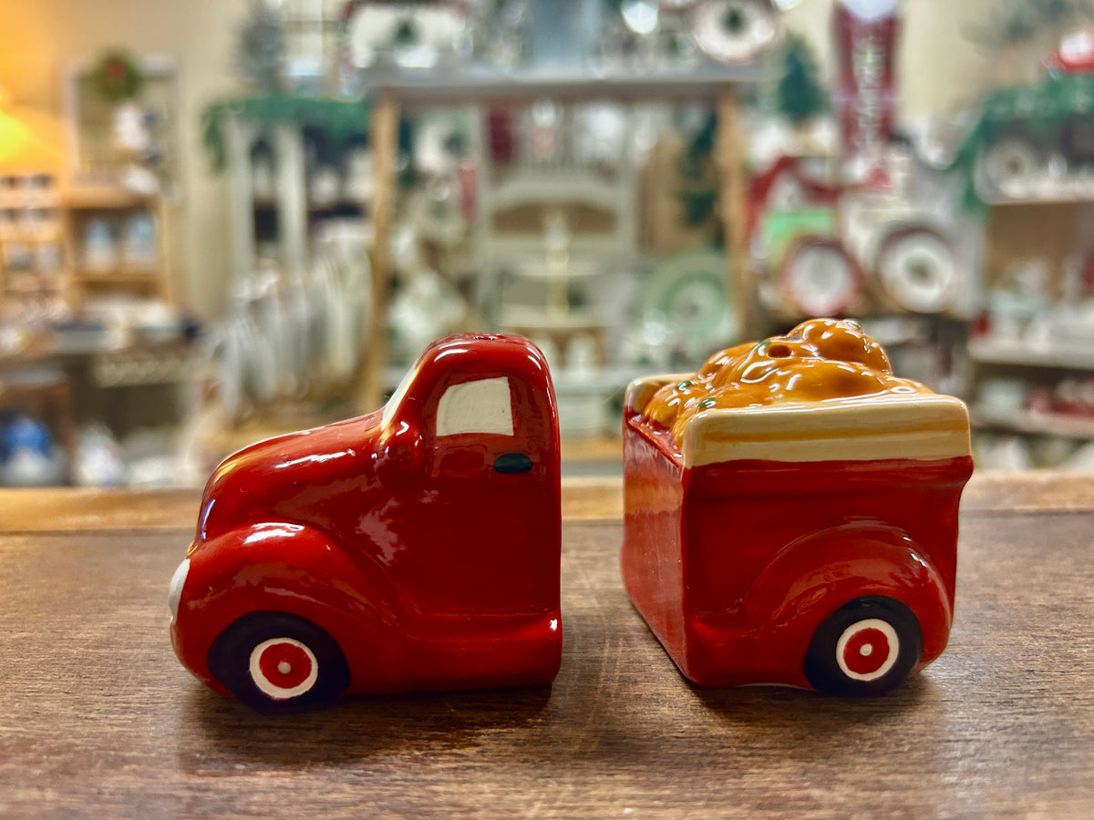 Small red ceramic truck figurine with white stripes and black wheels, side view.