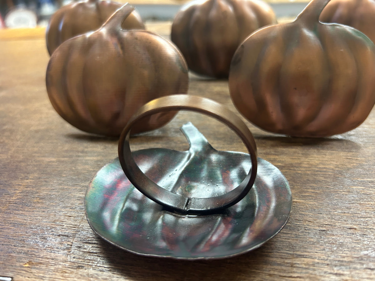 Copper pumpkin napkin ring detail with three pumpkin-shaped rings in background
