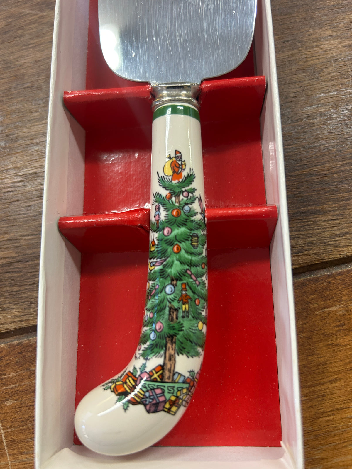 Red Christmas cake server handle with green tree scene and stainless steel blade