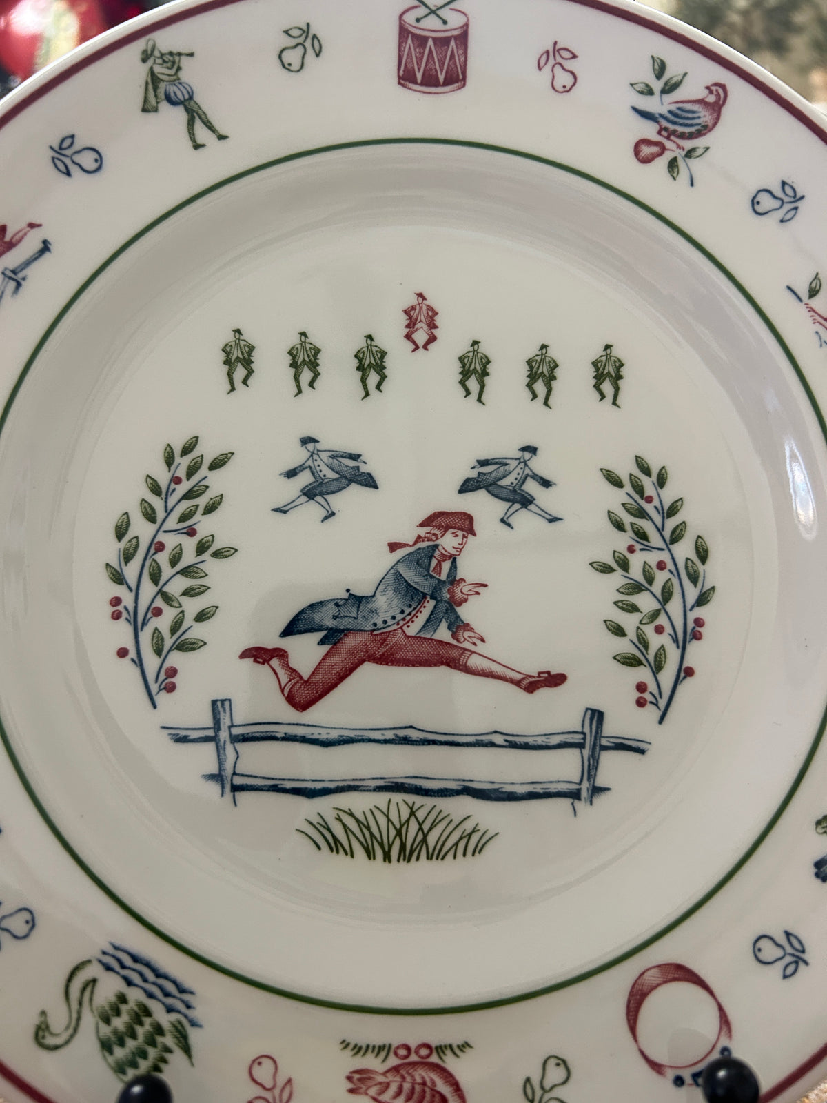 Multicolor Christmas plate showing horse rider, green figures, and floral rim accents