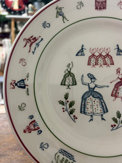 Multicolor Christmas plate showing girl and house figures with green vine border, white.
