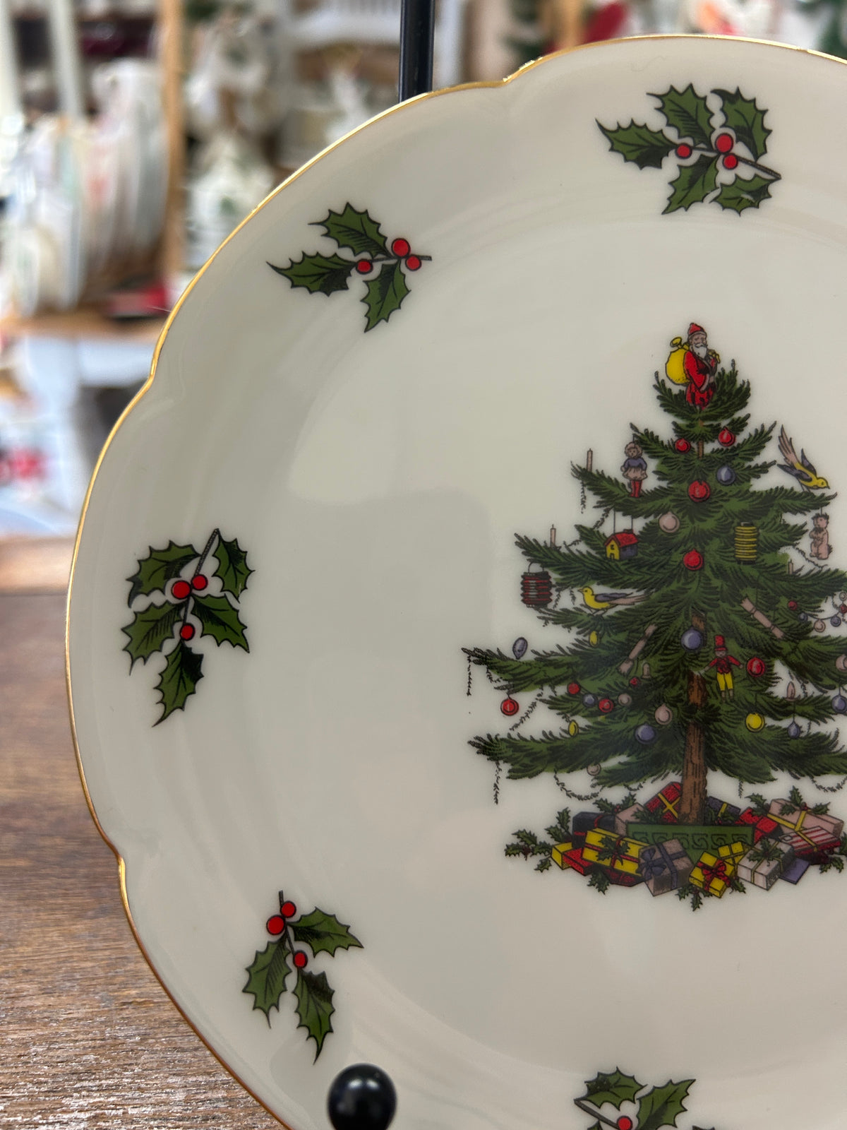White Christmas plate with gold edge, partial view of decorated tree and holly sprigs.