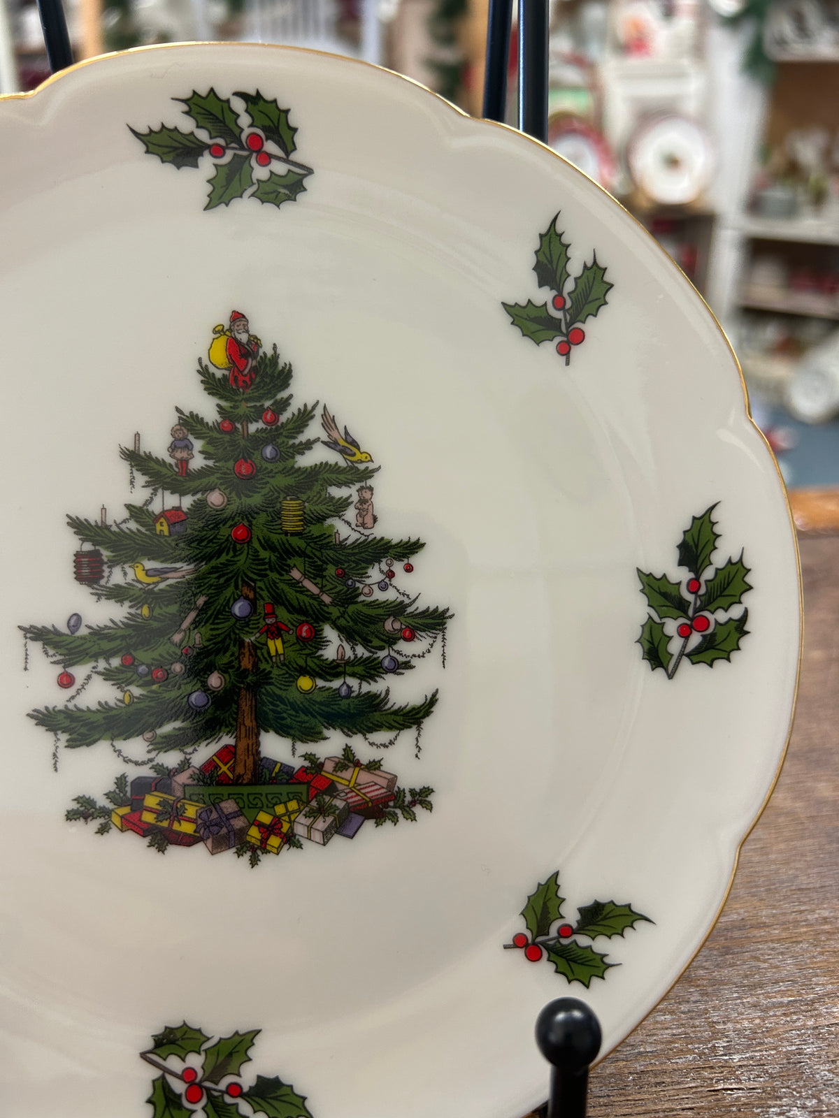 White Christmas plate on stand, illustrated tree with gifts and scattered holly sprigs.