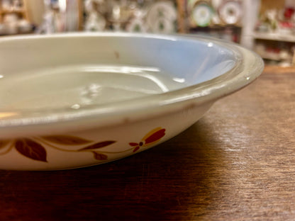 Side view of white ceramic pie plate with autumn leaf and flower accents in red and brown