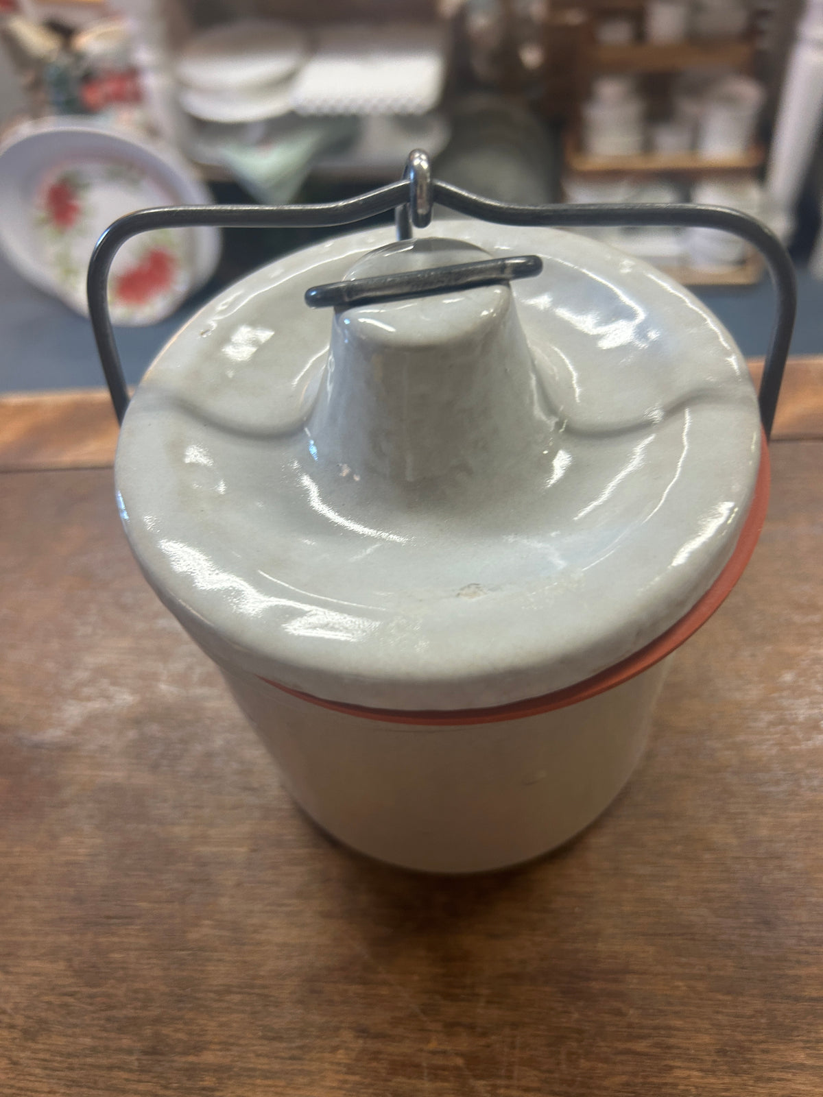 Cream stoneware crock with domed lid and raised knob beneath a dark metal latch handle