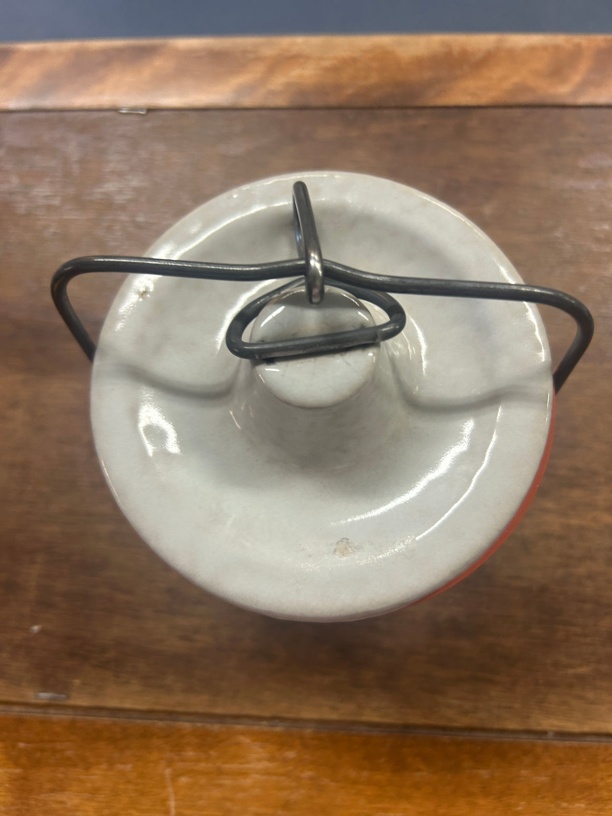 Top view of cream stoneware crock lid with raised knob and dark metal latch handle