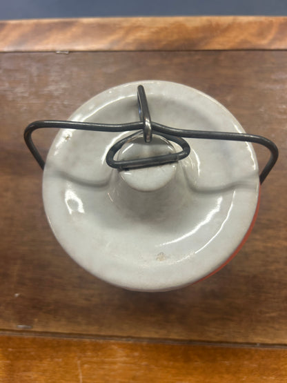 Top view of cream stoneware crock lid with raised knob and dark metal latch handle
