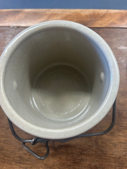 Open cream stoneware crock showing its glazed interior and dark metal latch handle
