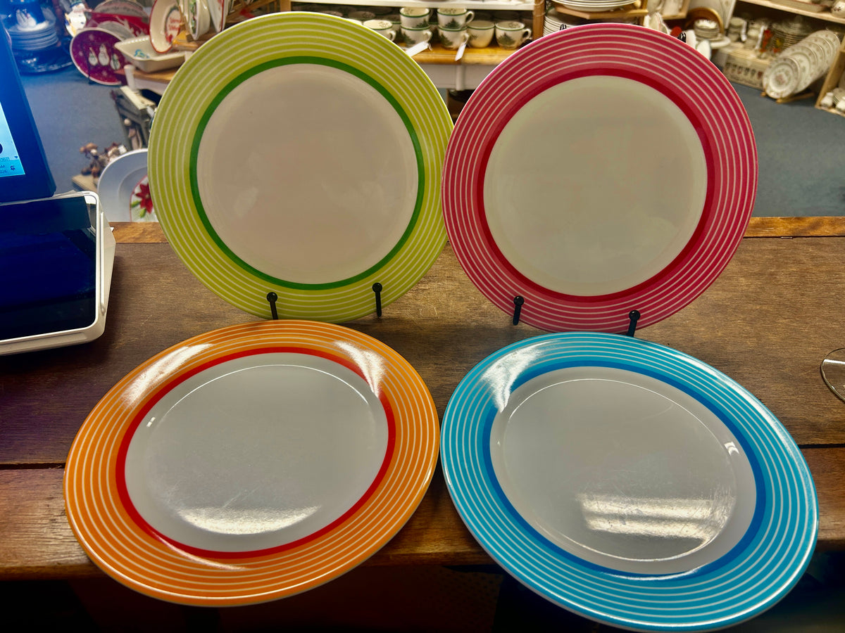 Four 9-inch melamine plates with white centers and striped rims in green, red, orange, and blue.