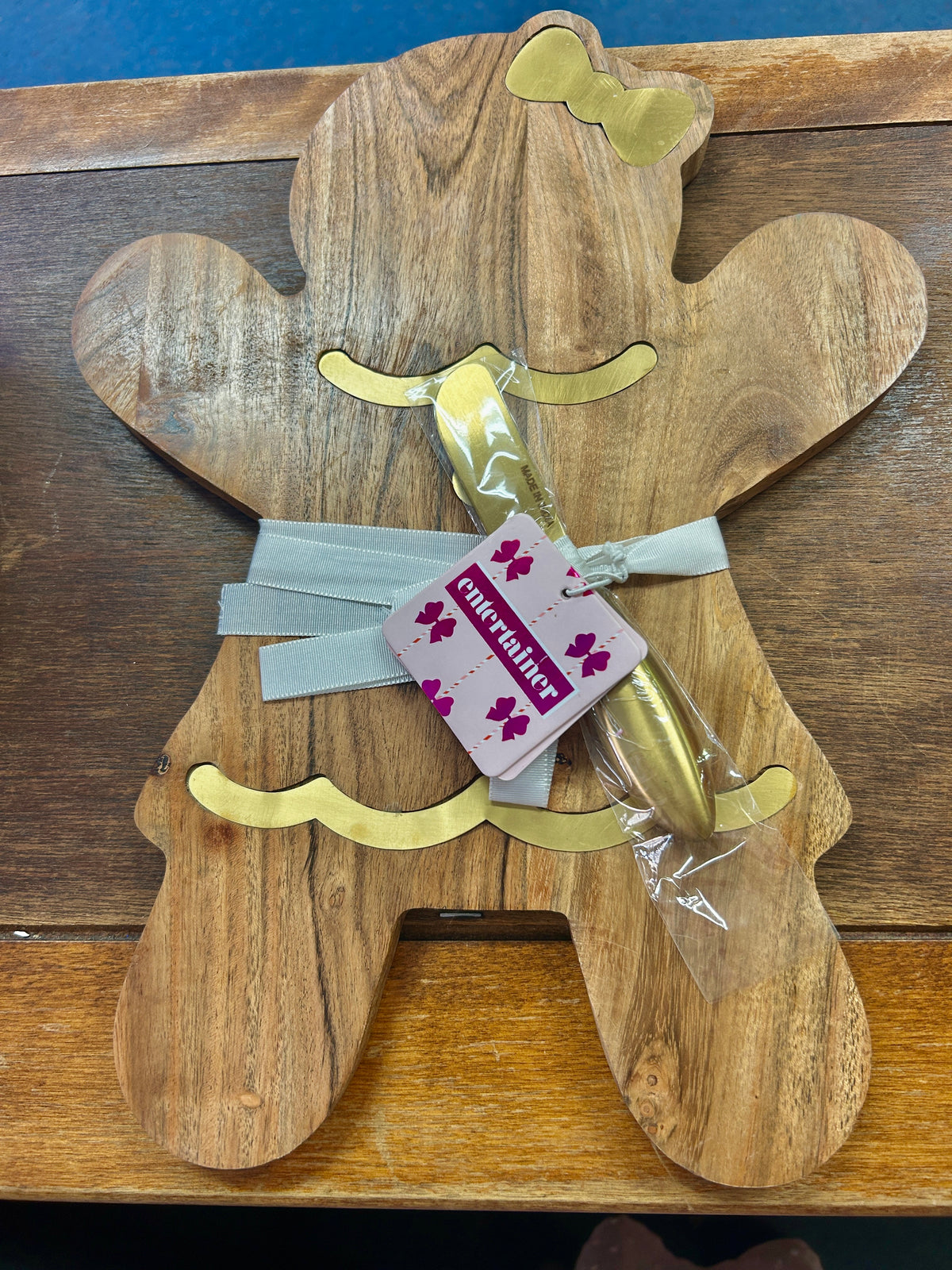 Gingerbread-shaped wooden serving board with gold accents and a wrapped spreader