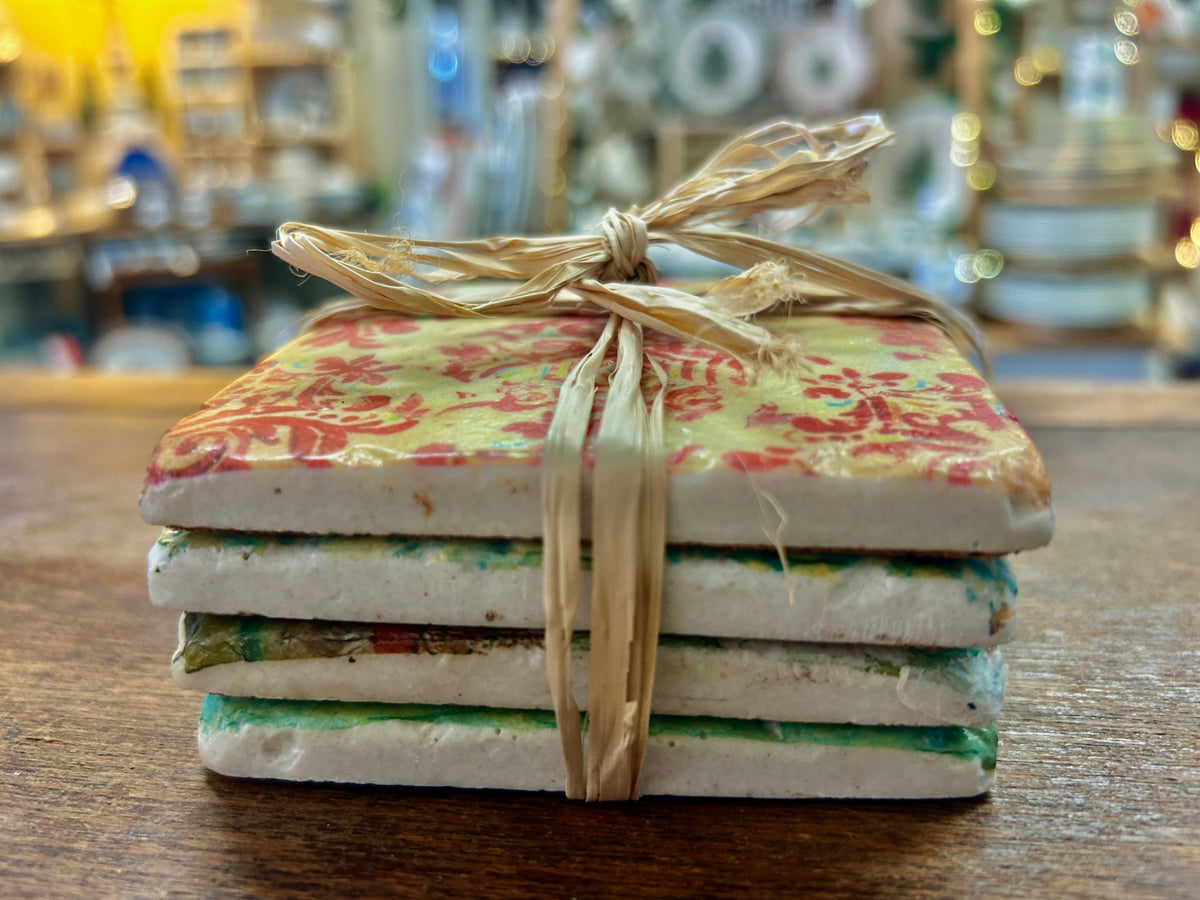 Set of four square stone coasters with colorful floral tops, tied with raffia