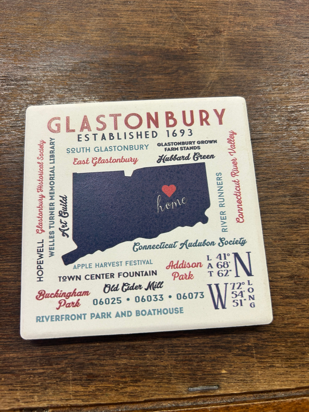 Square Glastonbury coaster with multicolor town names, landmarks, and a map design
