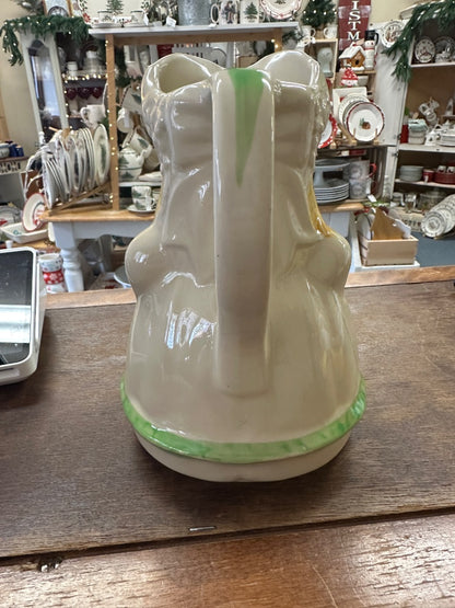 Ceramic pitcher back view with smooth white glaze, green base rim, curved handle