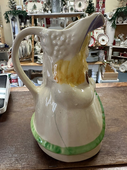 Ceramic pitcher angled view with painted bonnet, green base rim, curved handle