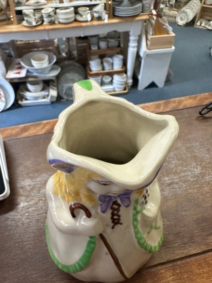 Ceramic pitcher with wide square mouth opening, painted doll details, green base rim