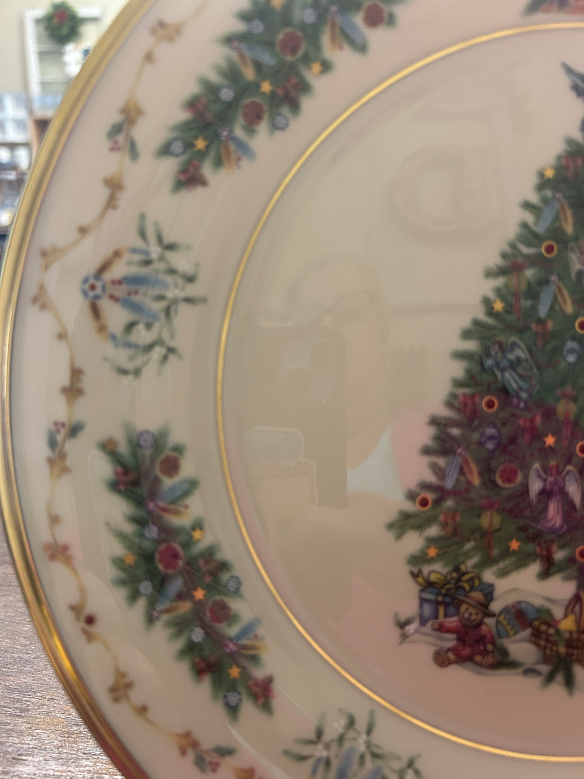 Christmas plate close-up: inner circle with painted tree scene, gold ring and garland border
