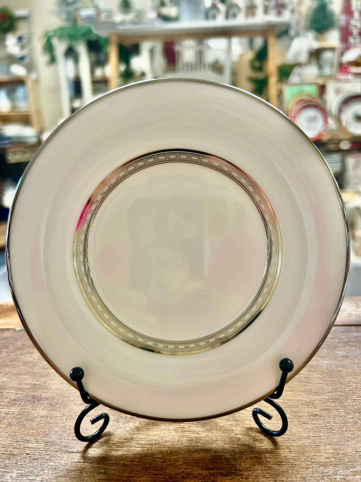 White saucer plate with gold rim and thin multicolor band, on black stand