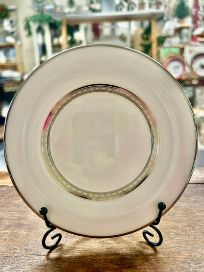 White saucer plate with gold rim and thin multicolor band, on black stand