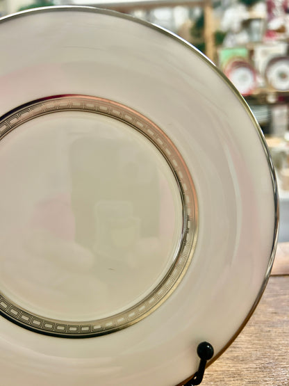 White saucer plate with gold patterned border and multicolor stripe