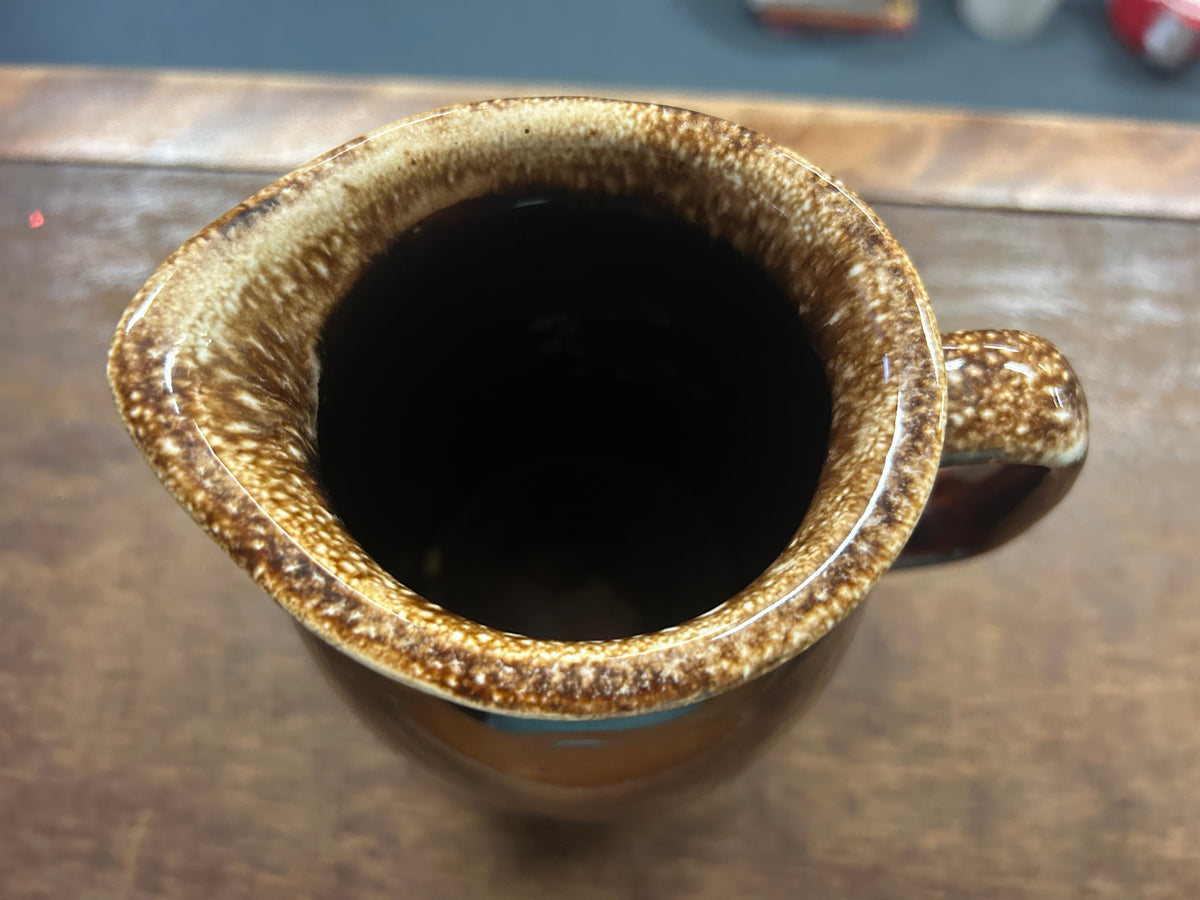 Brown ceramic pitcher opening with speckled glaze and side handle.