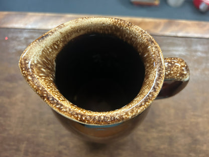Brown ceramic pitcher opening with speckled glaze and side handle.