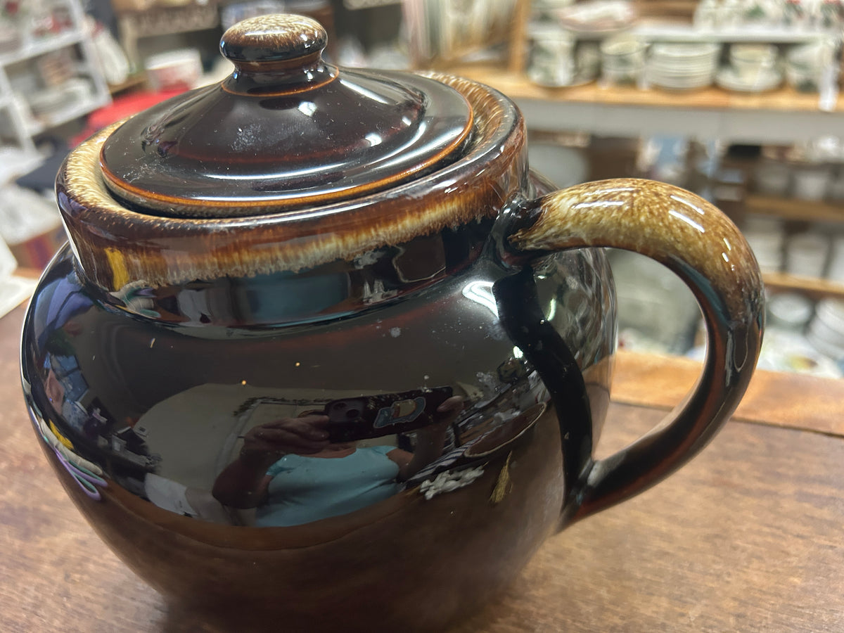 Brown glazed bean pot with fitted lid, gold-toned drip rim, side loop handle.