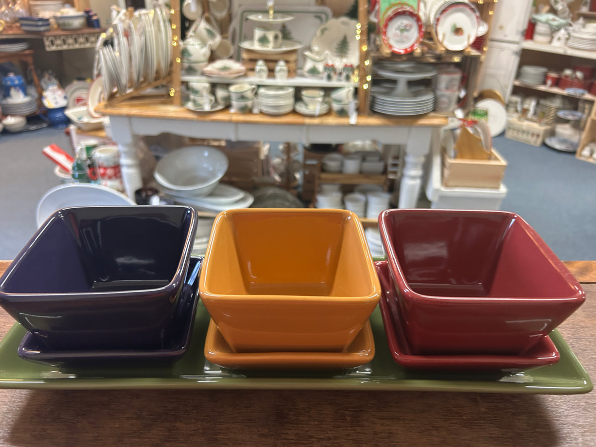 Three glossy square dishes (navy, orange, red) on a green serving tray