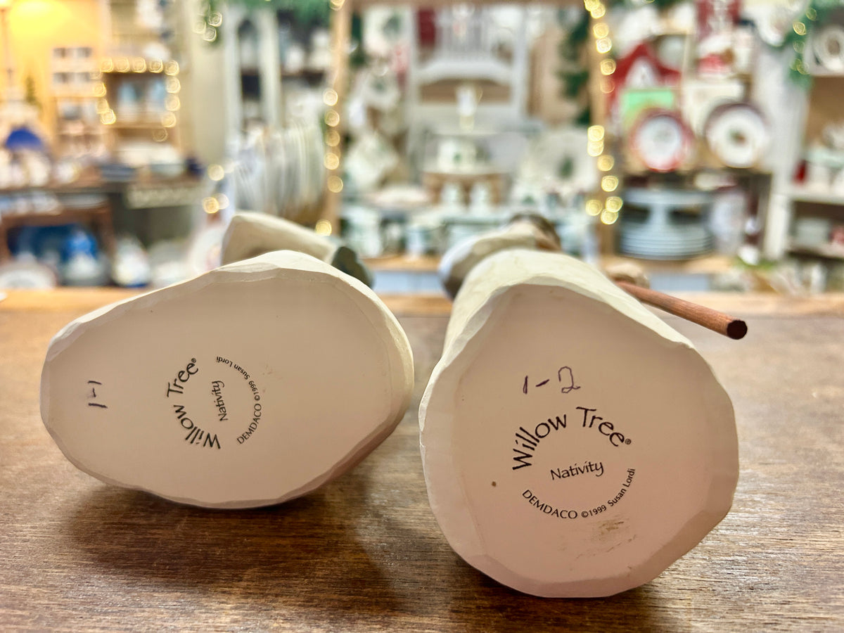 Bottom views of two cream nativity figurines with printed Willow Tree branding