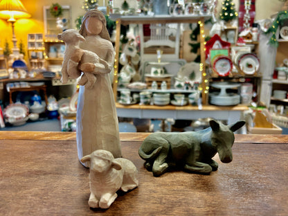 Cream nativity girl figurine holding sheep, with donkey figurine on wooden tabletop